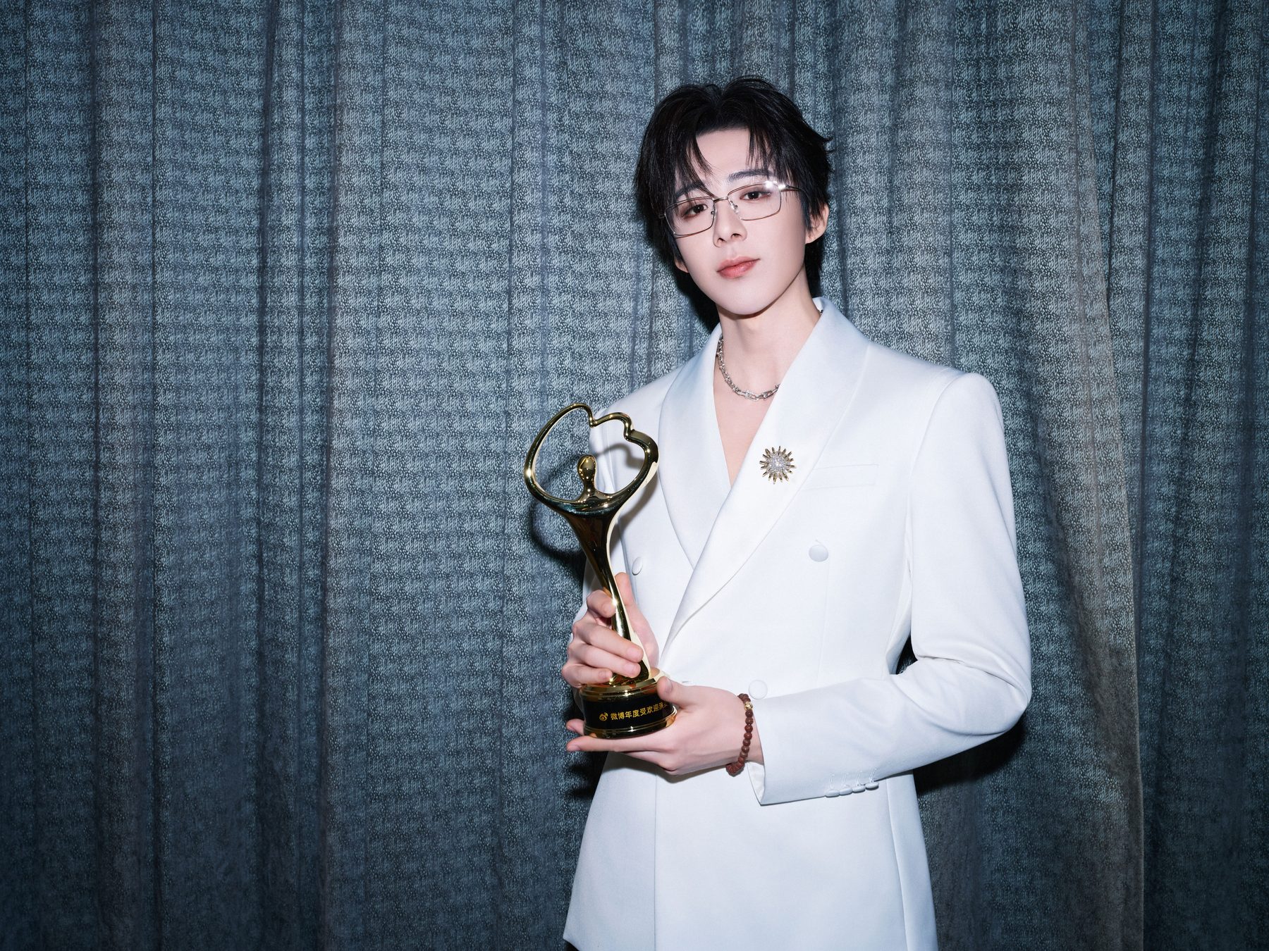 Liu Yuning in a white suit holding an award trophy